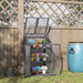 Grey 3-tier wooden mini greenhouse with potted flowers in a garden by a wooden fence
