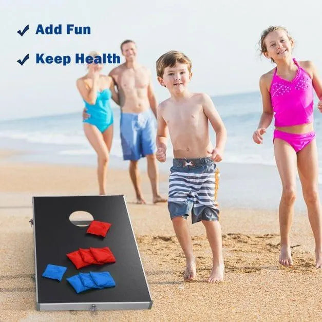 Family playing cornhole game board set on sandy beach, kids in swimsuits, ocean in background