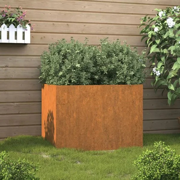 Corten steel garden planter with green shrubs on grass against wooden fence backdrop