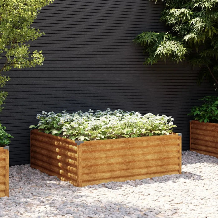 Corten steel raised garden bed with white flowering plants on gravel against black wall