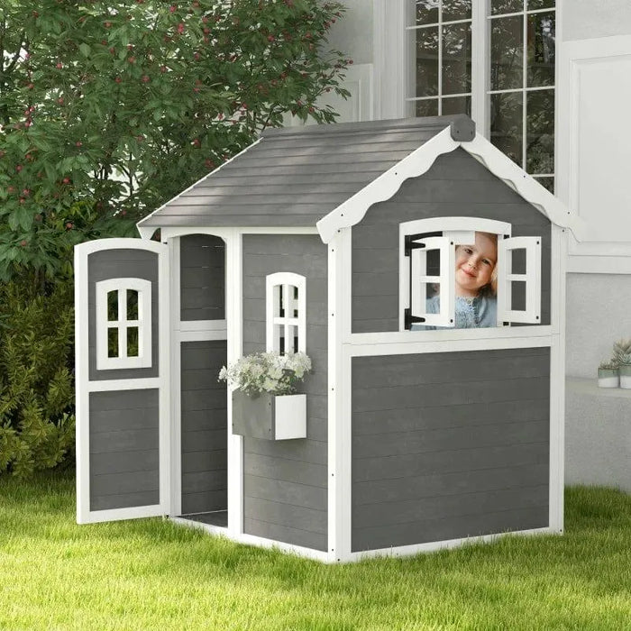 Grey wooden cottage-style playhouse with white trim, open door, flower box, and a child at the window.
