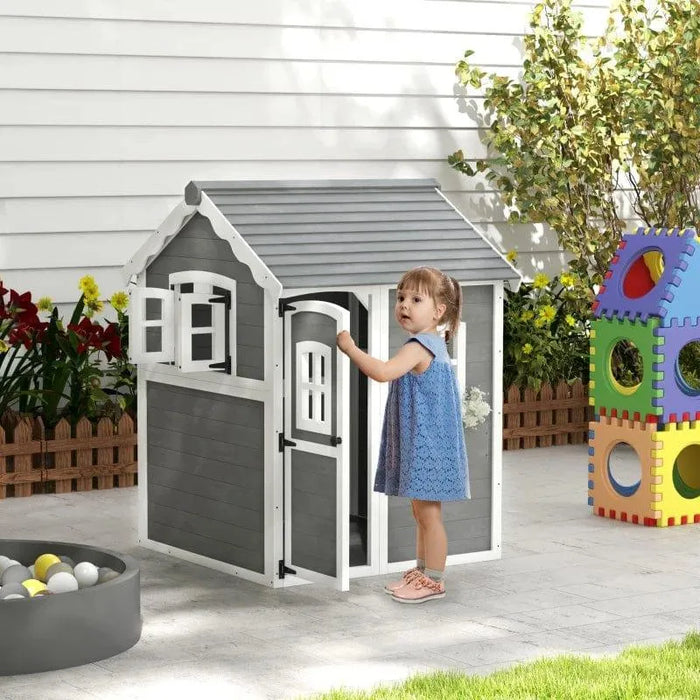 Child at grey wooden cottage-style playhouse in backyard with colorful outdoor toys