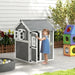 Child at grey wooden cottage-style playhouse in backyard with colorful outdoor toys