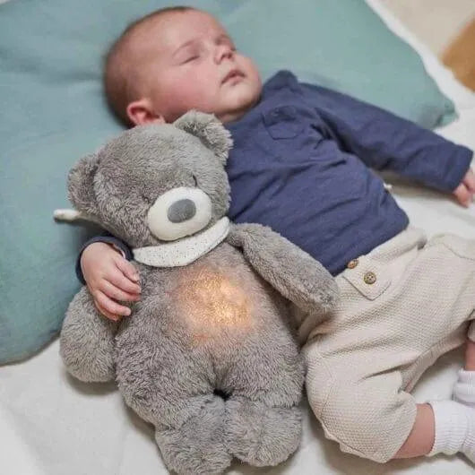 Sleeping baby cuddling grey cry-activated teddy bear night light on bed