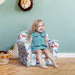 Smiling toddler sitting on multicolour dinosaur kids armchair in playful room