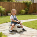Child riding a toy car on a stone path in a garden