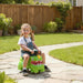 Child riding a green toy vehicle on a stone path in a garden