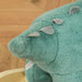 Close-up of plush dark green dinosaur rocking horse with grey felt spikes on wooden floor.