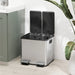 Modern double kitchen pedal bin with soft-close lids in stainless steel beside green cabinet and plant