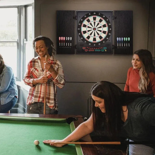 Group playing pool beside electronic LED dartboard with cabinet on wall