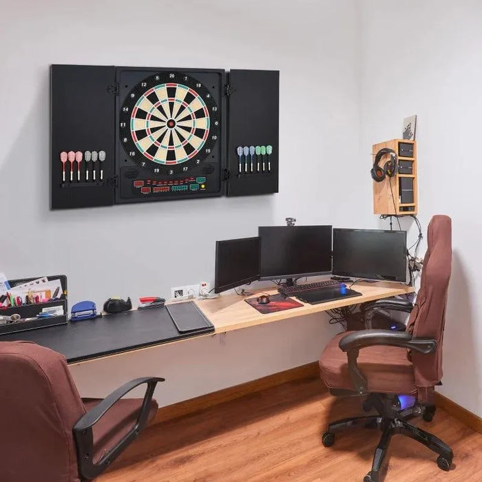 Electronic LED dartboard with cabinet and darts mounted above modern home office desk setup.