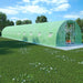 Extra long green polytunnel greenhouse with mesh cover on grassy lawn under blue sky