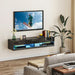 Black floating TV stand with LED lights under mounted 65-inch TV in modern living room with plant and wooden table
