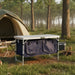 Foldable camping cupboard with storage, set up at a forest campsite near a tent.
