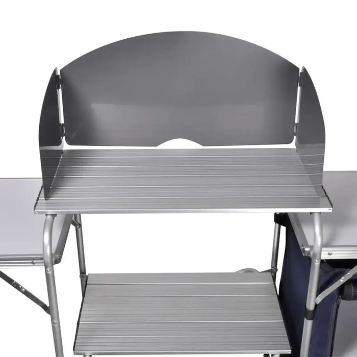 Foldable camping kitchen unit with metal shelves, windscreen, and side table.
