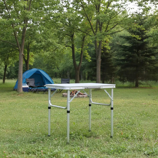 Lightweight aluminum folding camping table set up on grass with blue tent in background
