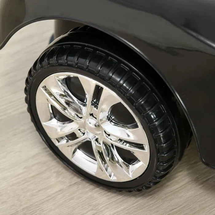 Close-up of shiny chrome wheel on black toddler ride-on car, indoor wood floor