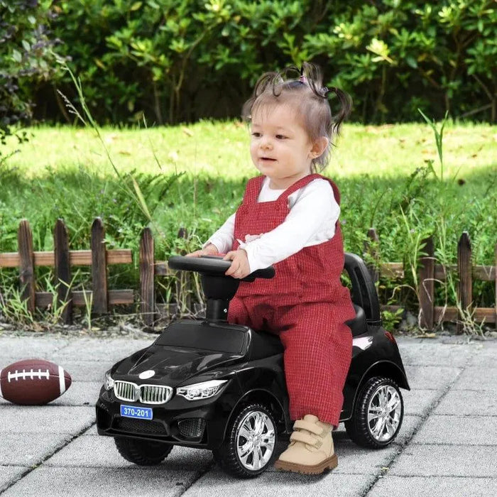 Toddler riding black foot-to-floor ride-on car with chrome wheels outdoors
