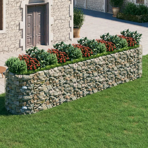 Gabion raised bed with galvanized iron and rock fill, planted with green shrubs and red flowers in a garden.