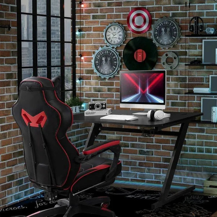 Black Z-shaped gaming desk with cable management, gaming chair, and brick wall decor