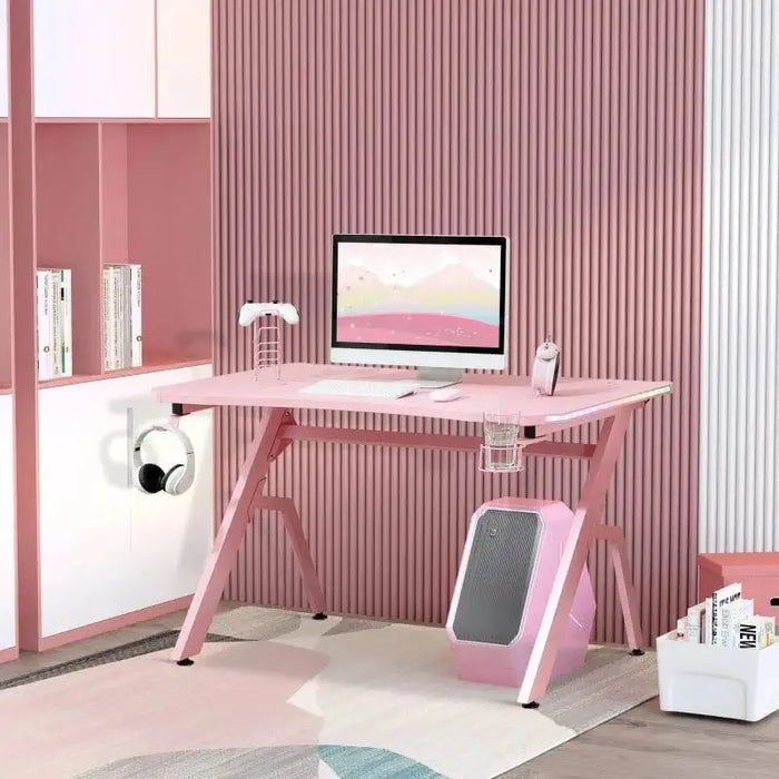 Pink gaming desk with monitor, accessories, and carbon fibre style in modern room setting