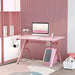 Pink gaming desk with monitor, accessories, and carbon fibre style in modern room setting