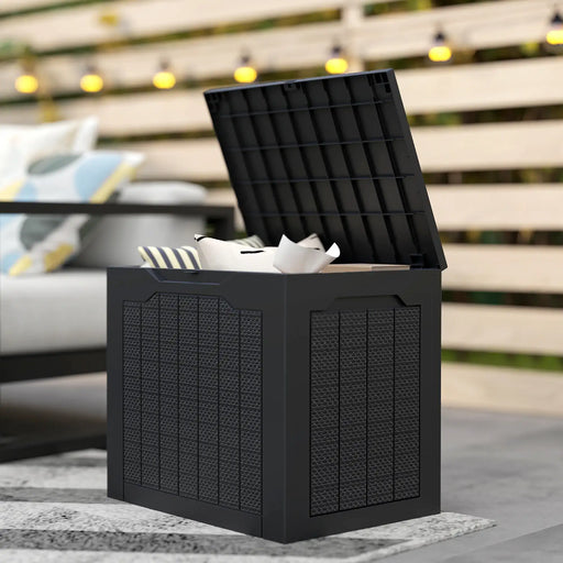 Black waterproof outdoor garden storage box with handles, open lid showing pillows inside, patio setting