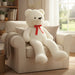Large white teddy bear with a red bow sitting on a beige armchair in a cozy living room.