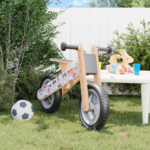 Grey and black adjustable balance bike with plywood frame on grass beside a soccer ball and toys.