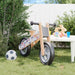 Grey and black adjustable balance bike with plywood frame on grass beside a soccer ball and toys.