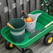 Heavy-duty green garden dump cart with pot, bucket, spray bottle, and shovel on wooden deck