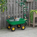 Heavy-duty green garden dump cart with gardening tools on patio by wooden fence and flowers