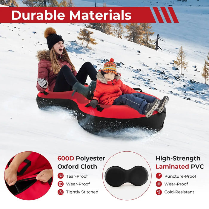 Two people sledding on a red and black inflatable snow tube on a snowy hill with winter gear