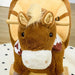 Brown plush rocking horse with foot pedals and wooden handles on a light rug
