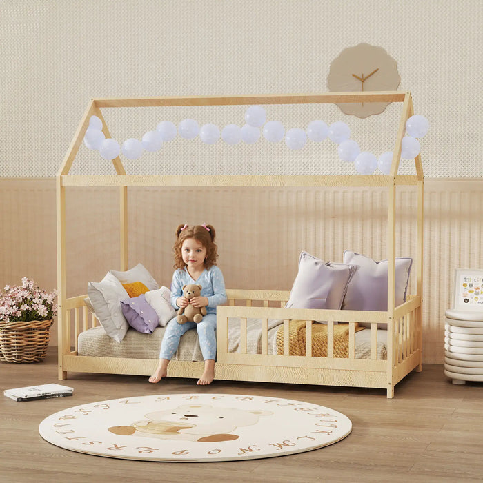 Child sitting in a wooden crib with a teddy bear in a room with balloons and a clock.