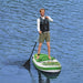 Man paddleboarding on inflatable green and white SUP in calm blue water