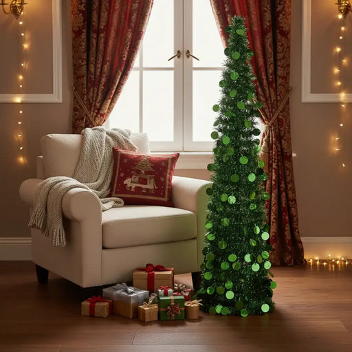 Small green sequin Christmas tree next to armchair with knitted blanket and red pillow, gifts below