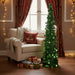 Small green sequin Christmas tree next to armchair with knitted blanket and red pillow, gifts below