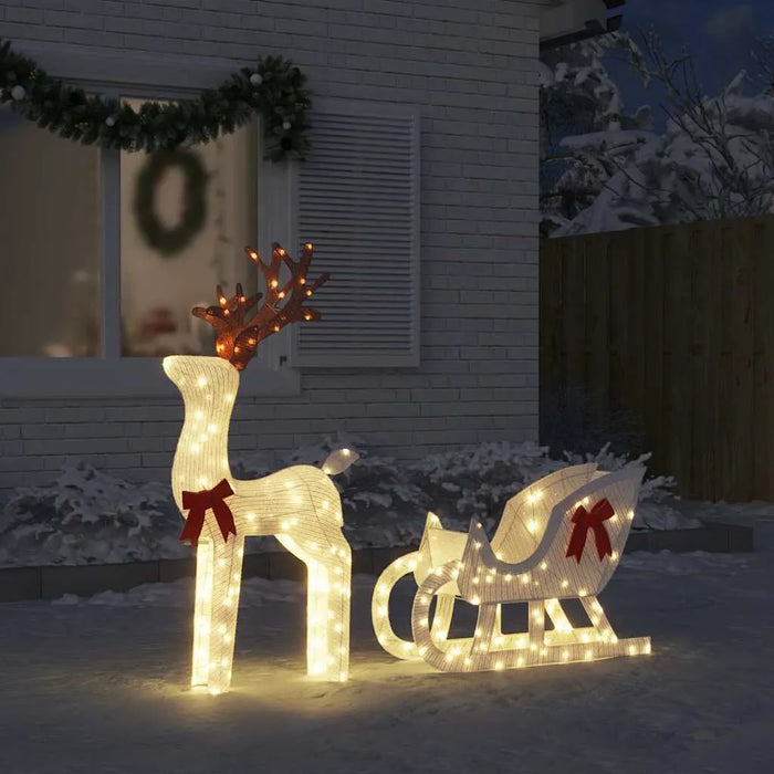 Illuminated Christmas reindeer and sleigh decoration with red bows in snowy yard at night