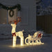 Illuminated Christmas reindeer and sleigh decoration with red bows in snowy yard at night
