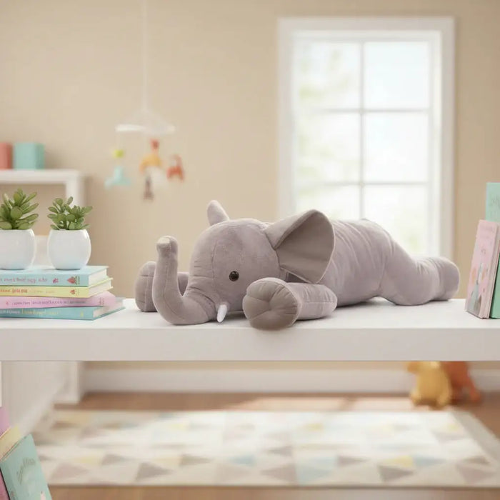 Gray elephant plush toy on a white surface in a room with books and plants.