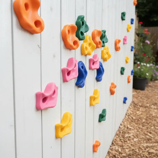 Colorful climbing holds attached to white wooden fence for outdoor kids rock climbing wall
