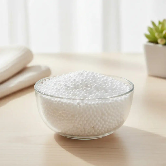 Glass bowl filled with white foam beads on a wooden surface with folded cloth and potted plant