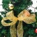 Green Christmas tree decorated with gold ribbon bow and shiny gold and red baubles