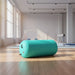 Teal cylindrical fitness roller on wooden gym floor with large windows and exercise equipment in background