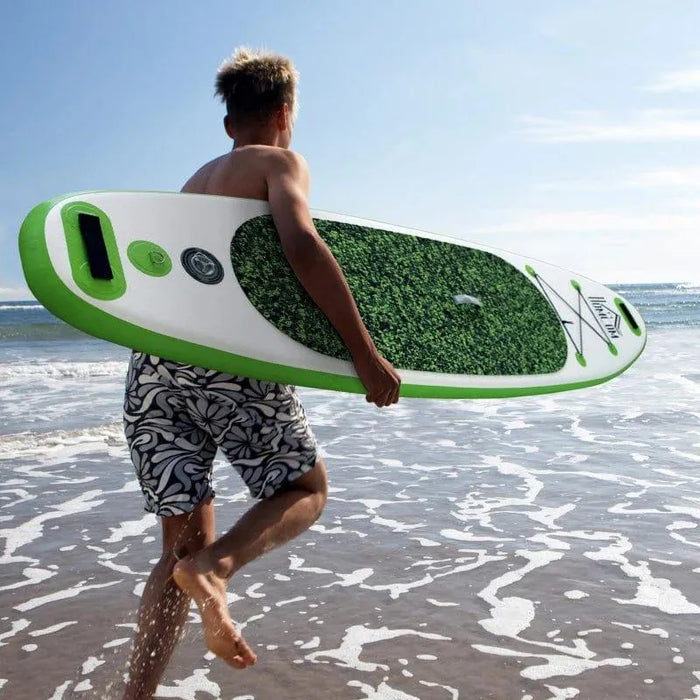 Person carrying green inflatable paddleboard on a sunny beach shoreline