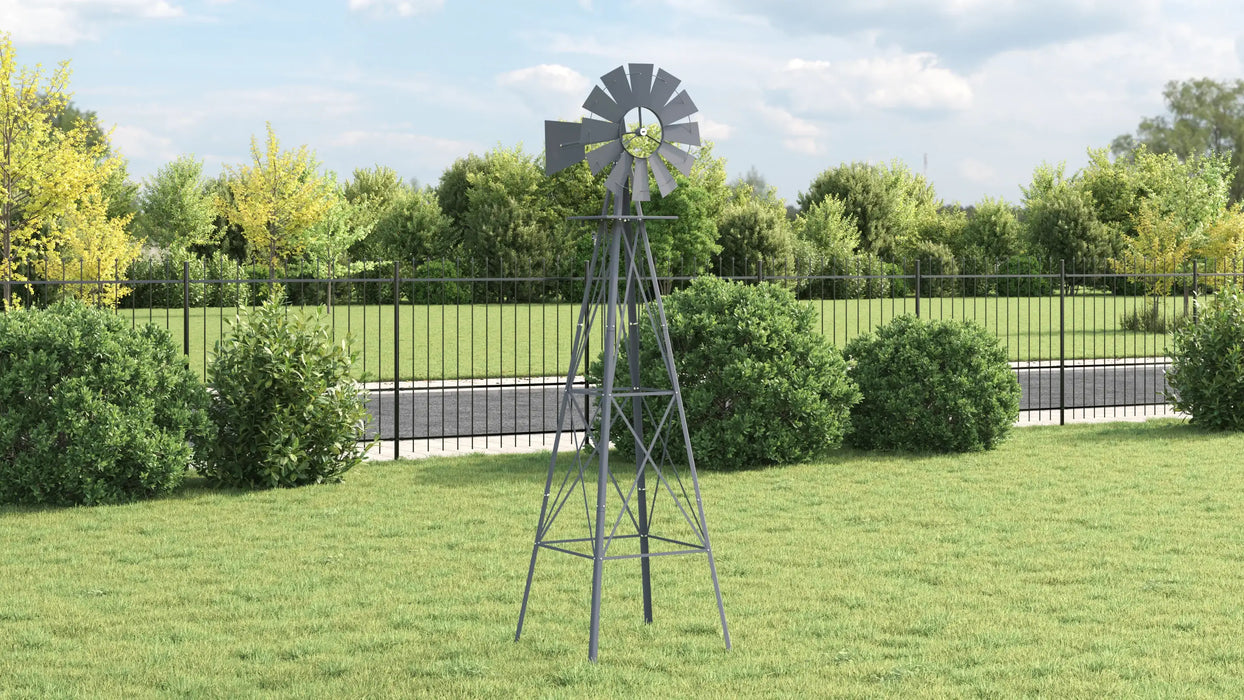 Metal windmill on a grassy area with trees and a fence in the background