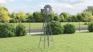 Metal windmill on a grassy area with trees and a fence in the background