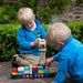 Two young boys in blue jackets playing outdoors with a colorful wooden toy container ship CMA CGM