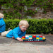 Young boy in blue jacket playing on stone patio with magnetic wooden toy container ship outdoors